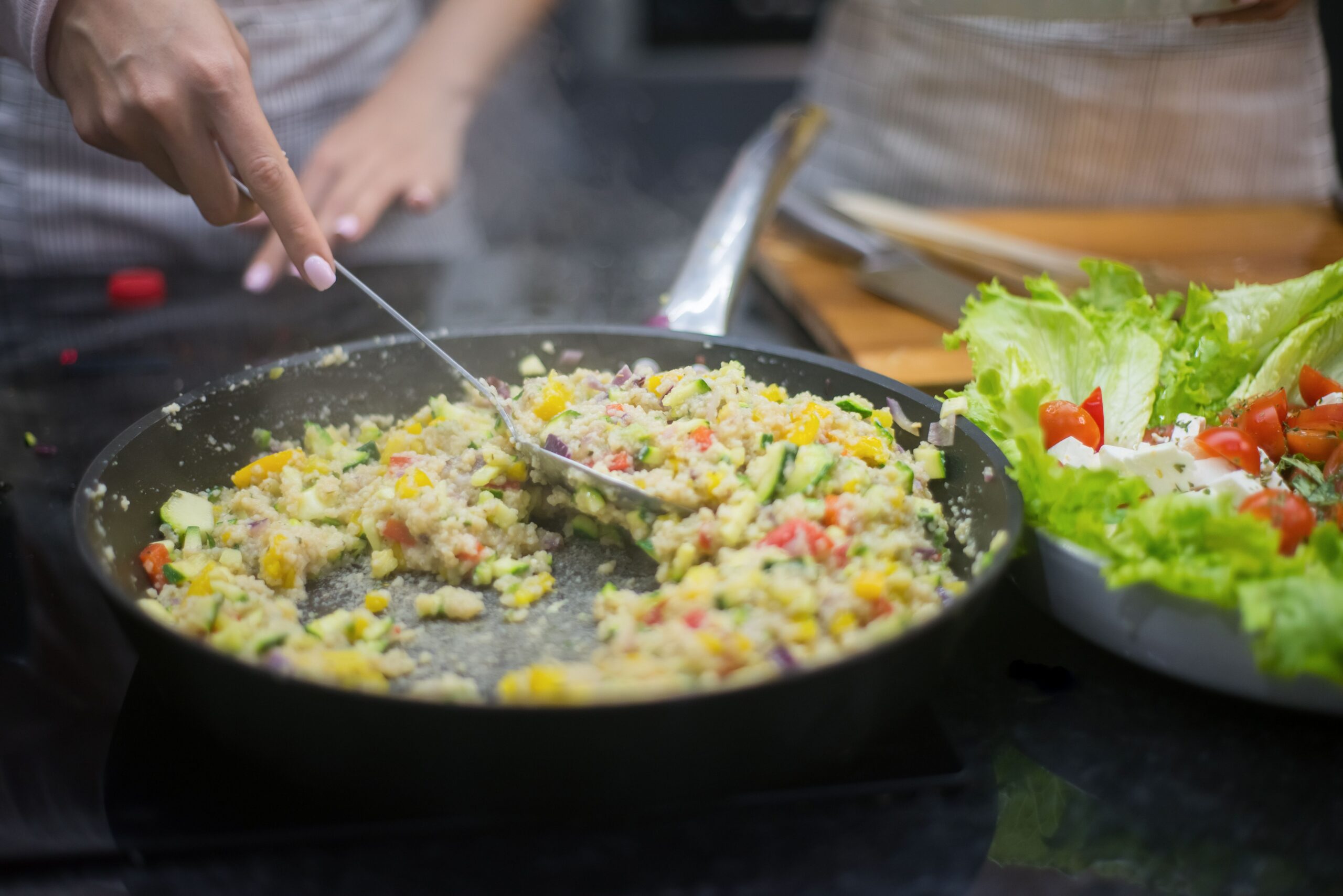 Fresh vegetable stir-fry in a pan with lettuce salad, captured in a kitchen setting.